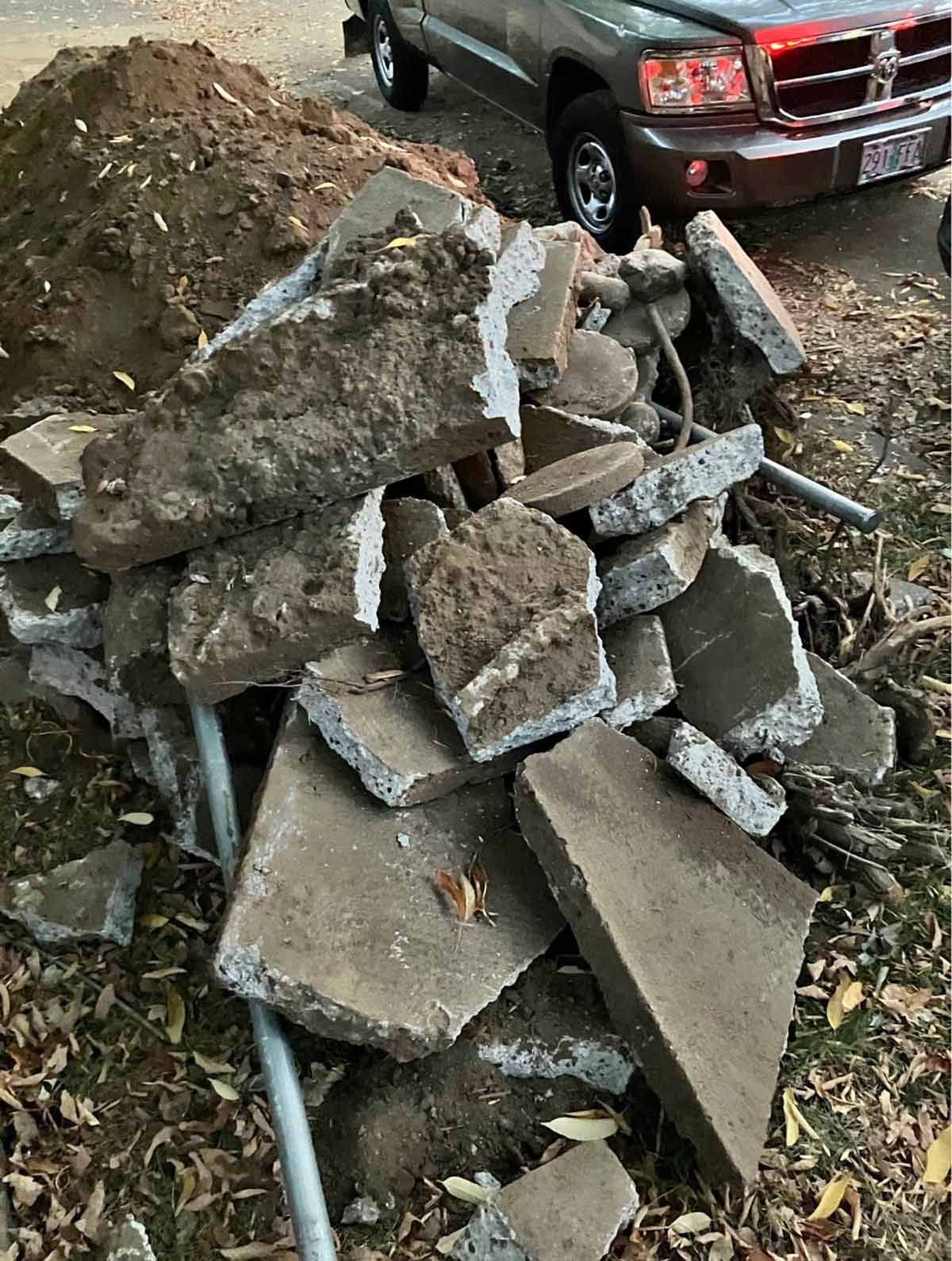 Pile of broken concrete slabs and metal pipes beside a red pickup truck outdoors.