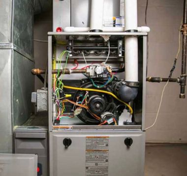 Hand connecting a pipe under a wall-mounted gas water heater with exposed valves and hoses
