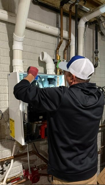 Technician wearing gloves inspects open HVAC unit in a utility room with exposed pipes