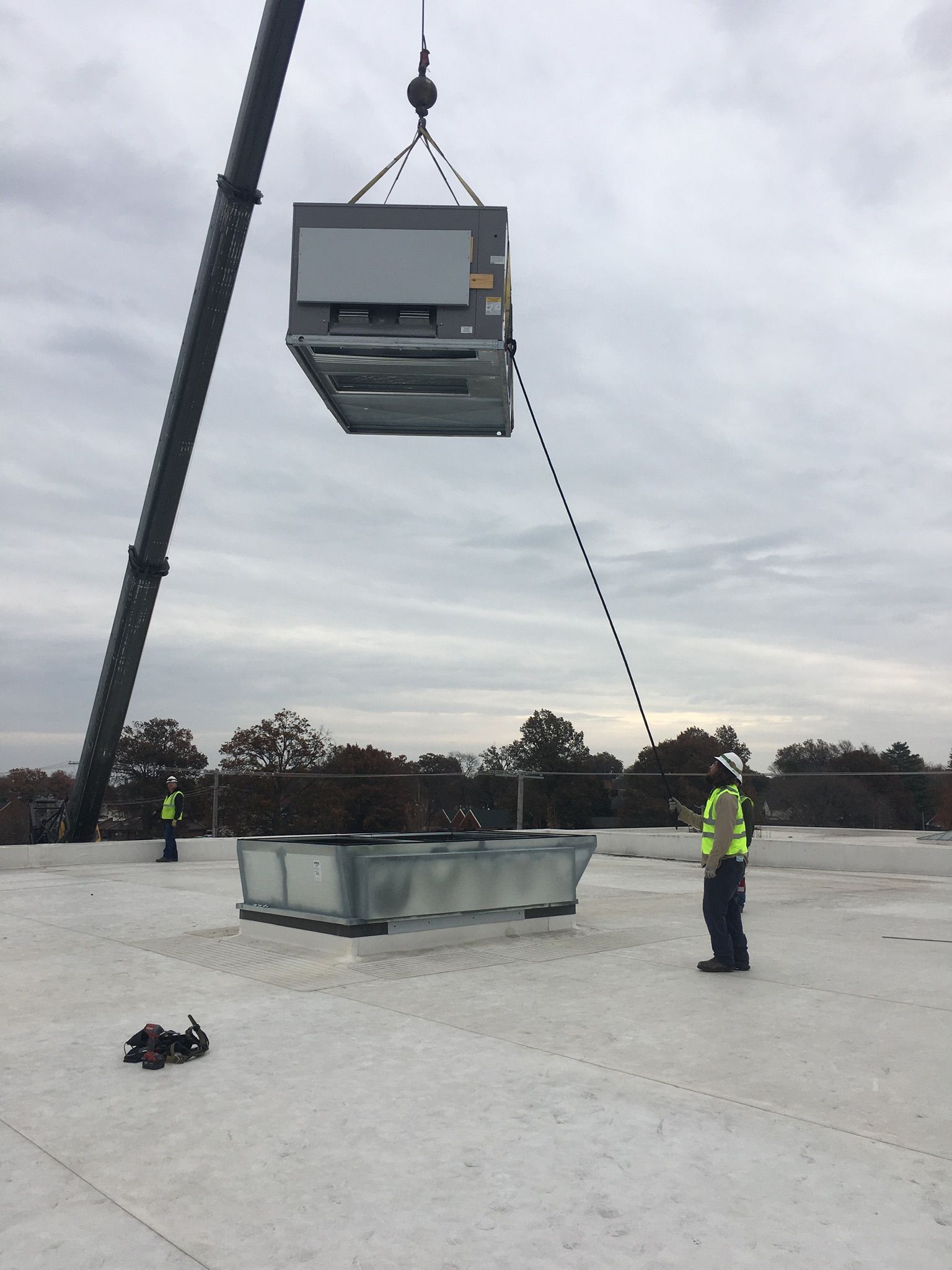 Crane lifting stacked gray containers on a concrete lot while a worker in a hi-vis jacket supervises.