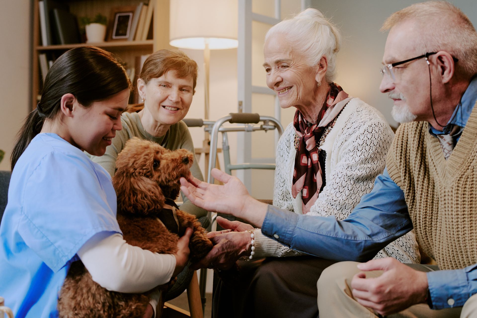 Caregiver and three seniors interacting with a small brown dog in a cozy living room Caregiver and three seniors interacting with a small brown dog in a cozy living room