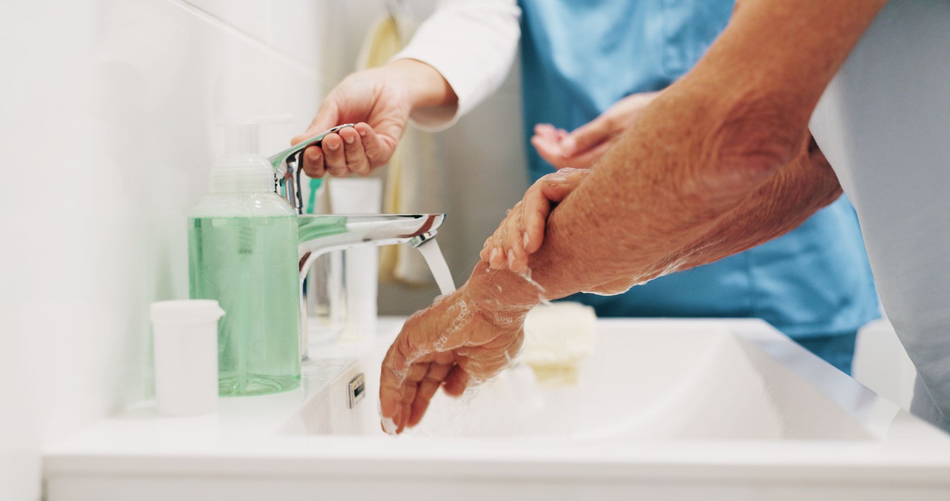 Person washing hands at a bathroom sink with green soap dispenser Person washing hands at a bathroom sink with green soap dispenser