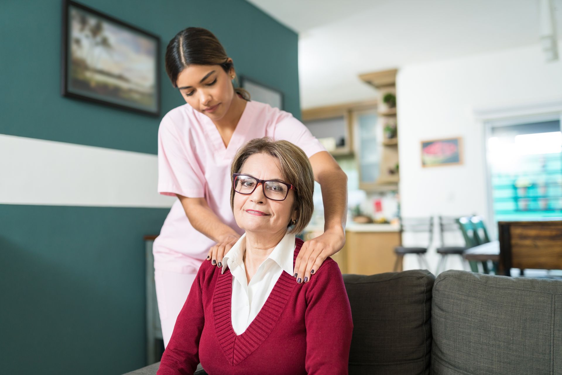 Caregiver gently adjusting an older woman’s hair on a couch in a bright living room
