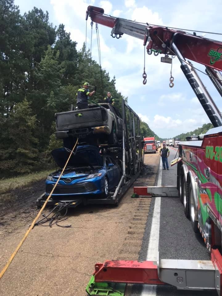 Tow truck lifting a damaged blue car on a highway shoulder after a crash