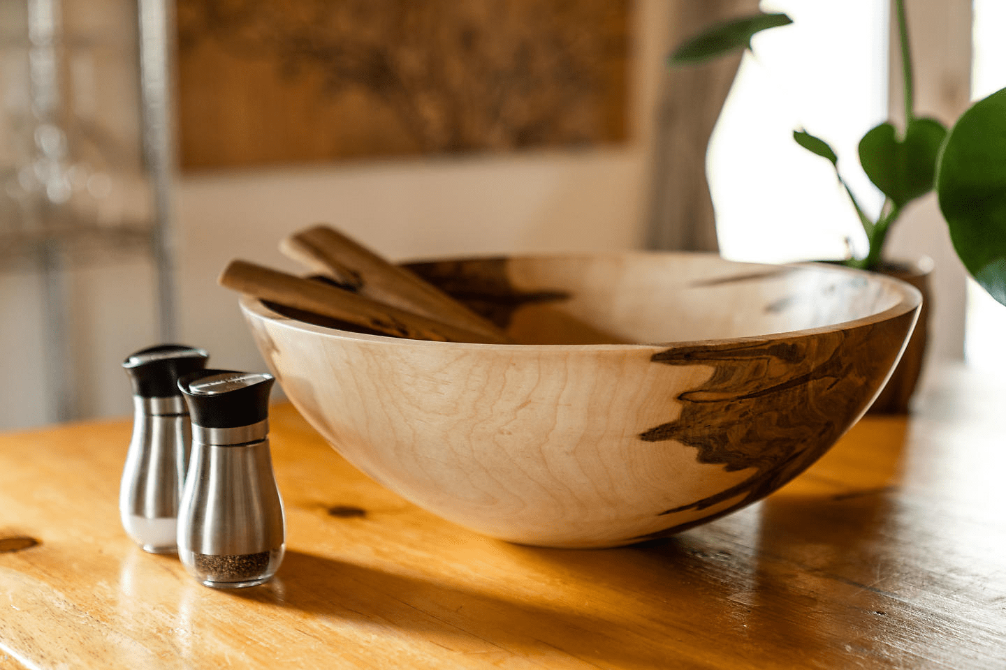 Wooden bowl with utensils on a table, beside a small salt and pepper set