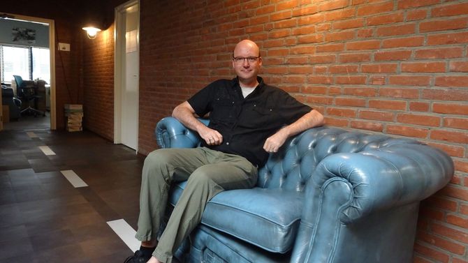 De eigenaar zit op een gecapitonneerde blauwe leren bank tegen een bakstenen muur in een kantoor.