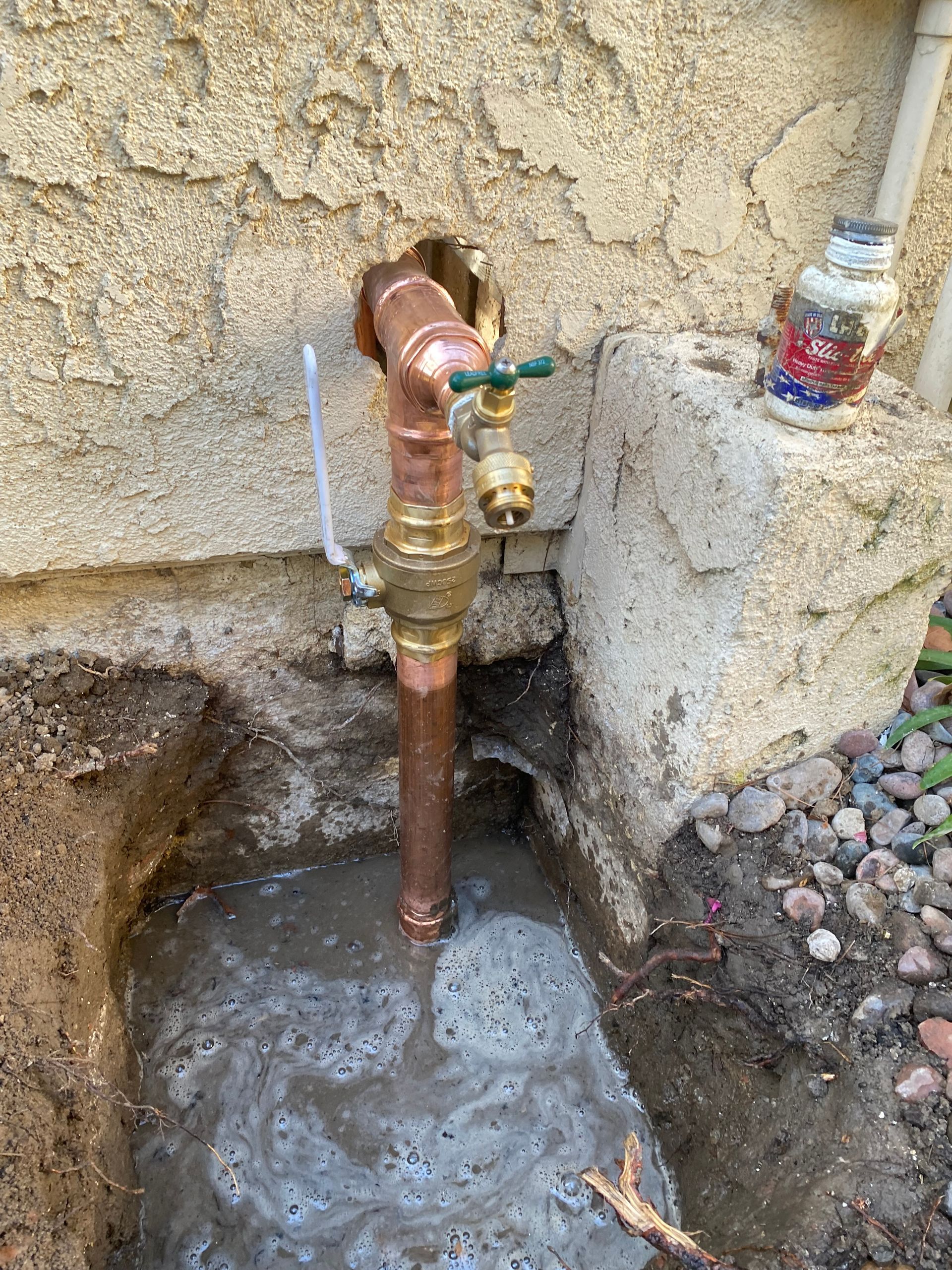 A copper pipe is sitting in a hole in the ground next to a wall.