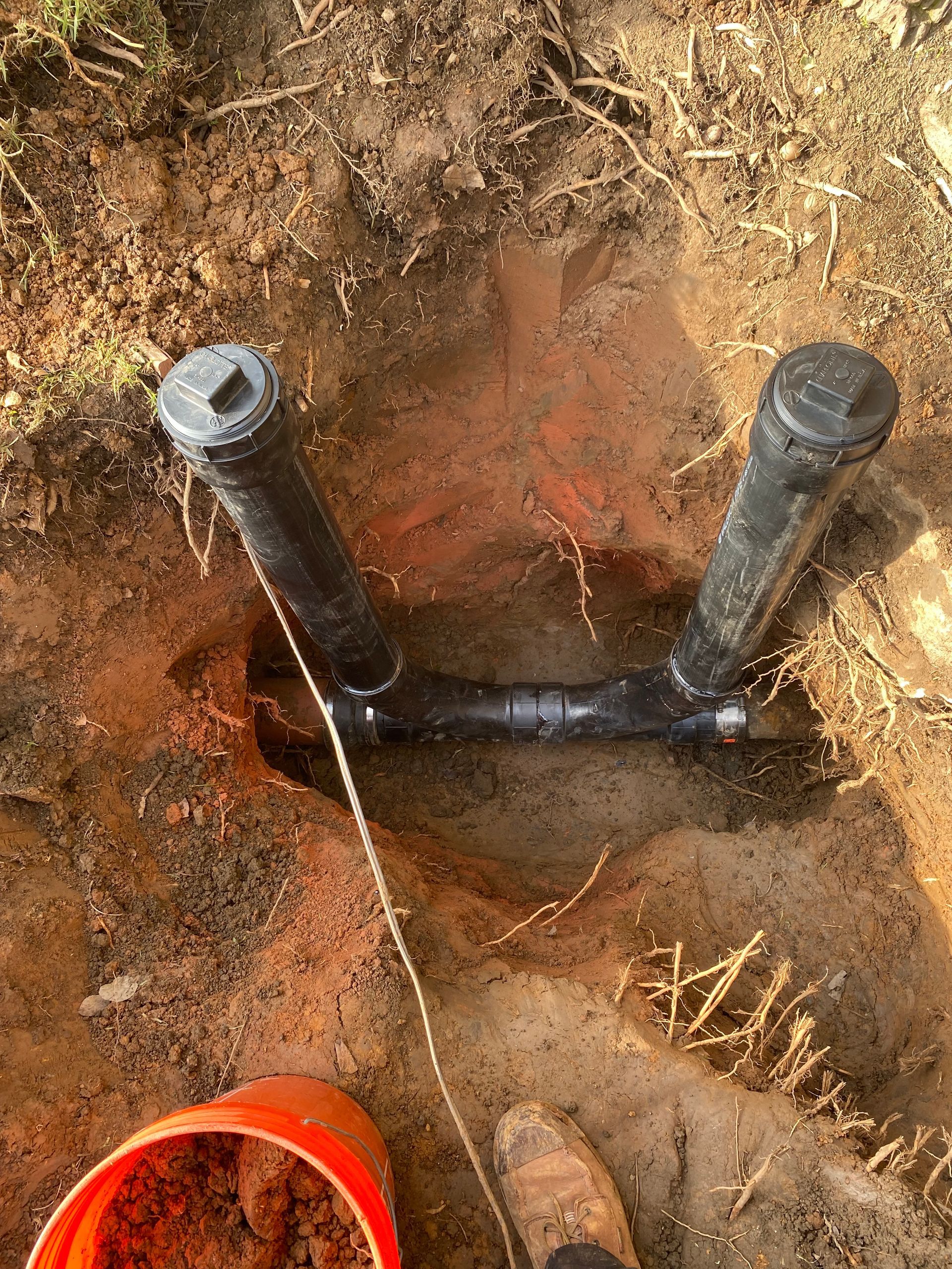 A pipe is sitting in the dirt next to a bucket of dirt.