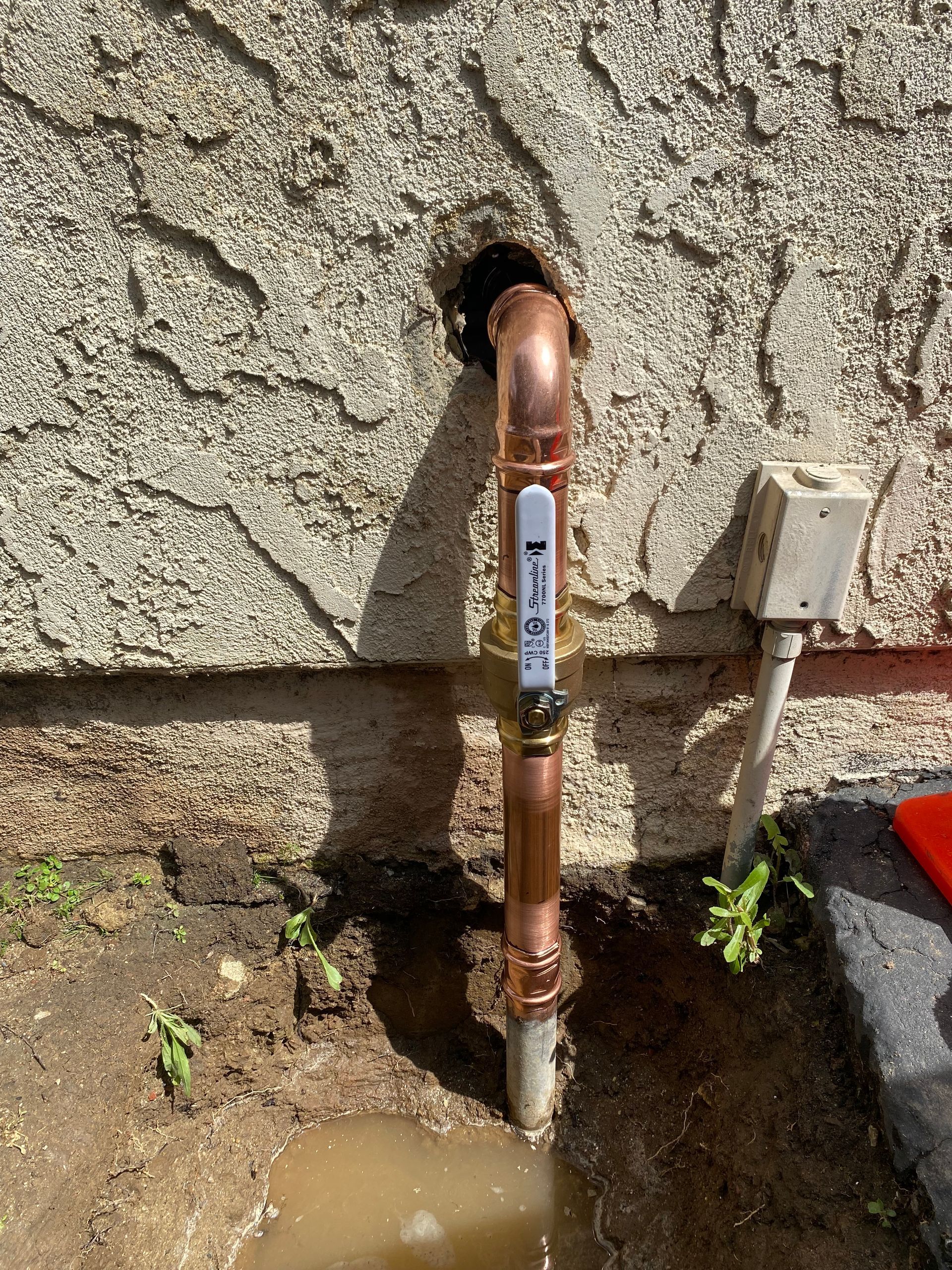 A copper pipe is sitting in the dirt next to a wall.