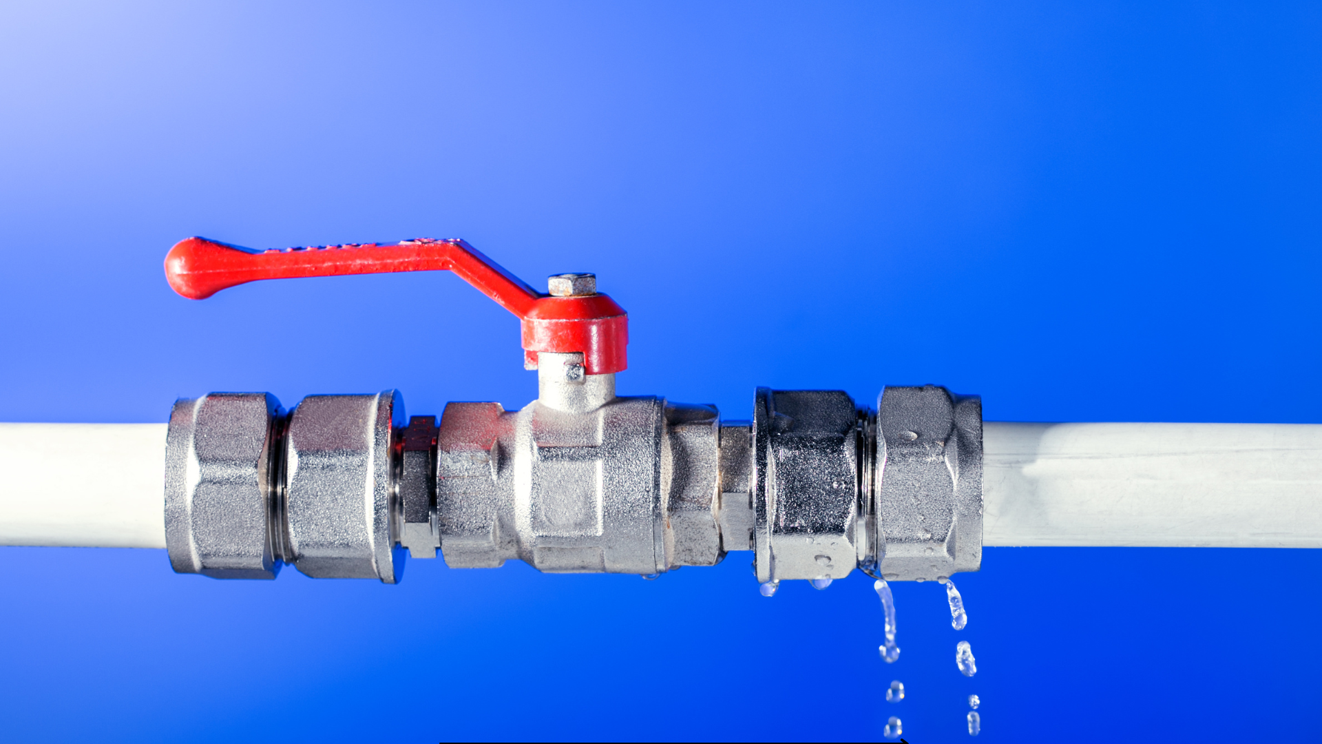 A water pipe with a red valve is leaking water.