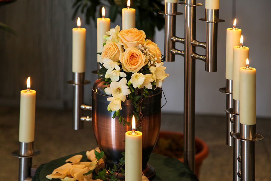 A urn with flowers and candles is on a table.