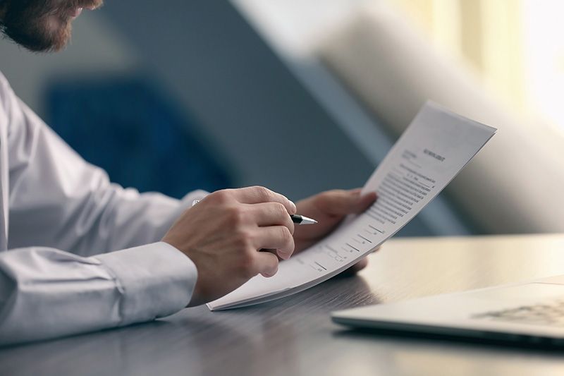 A man is sitting at a table writing on a piece of paper with a pen.