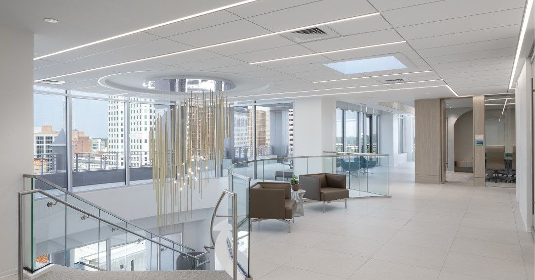 Bright, modern office interior with a glass staircase, seating area, and city view.