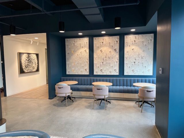 Modern seating area with blue walls, artwork, small tables, and pink chairs. Concrete floor.