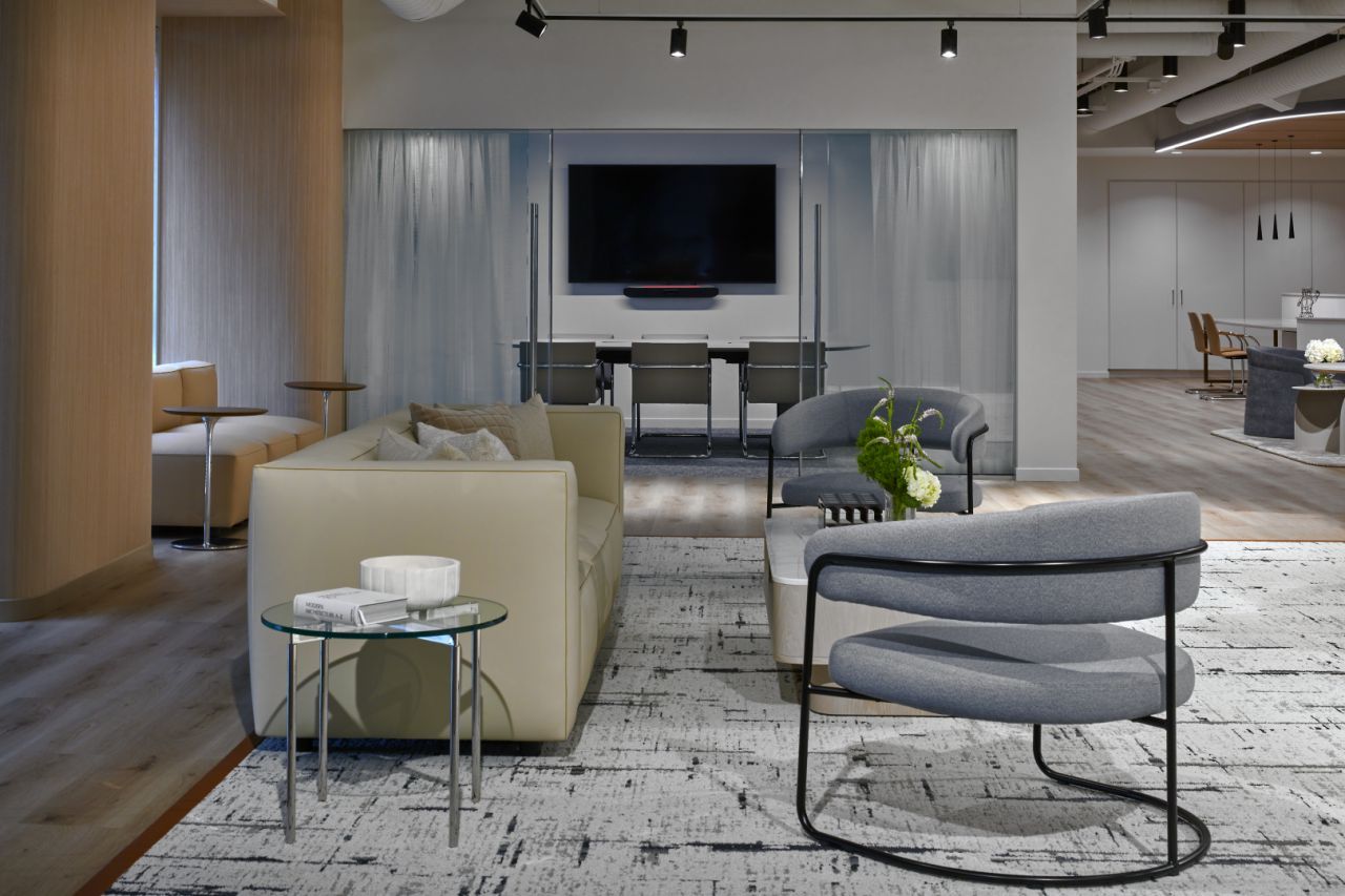 Modern living room with neutral colors, a sofa, and gray chairs, with a dining area in the background.