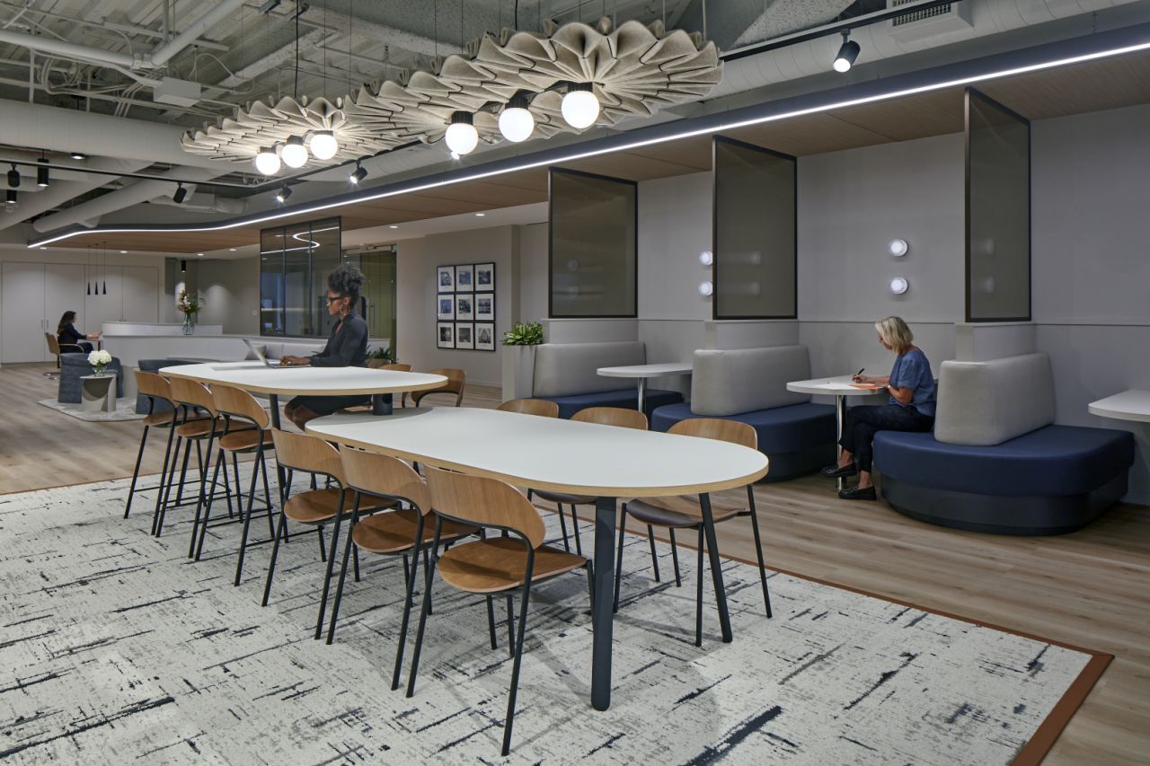 Modern office with tables and chairs, two people at tables, booths, and decorative lighting.