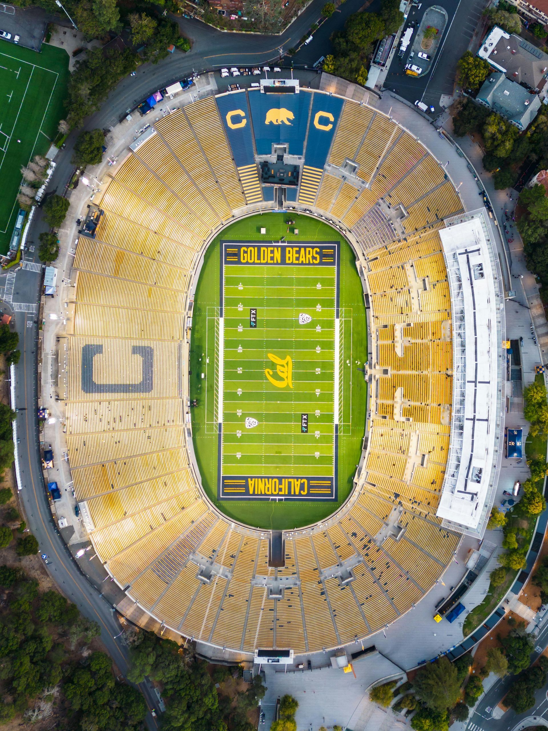Aerial view of California Memorial Stadium, yellow and blue, with a football field.