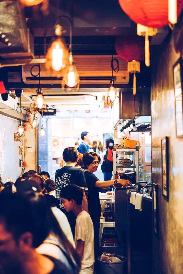 Crowded narrow restaurant corridor with hanging lights and people waiting near the counter
