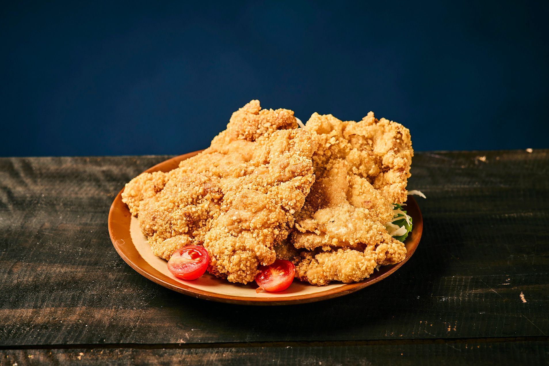 A plate of crumb-covered fried dessert with strawberries on a dark wooden table.