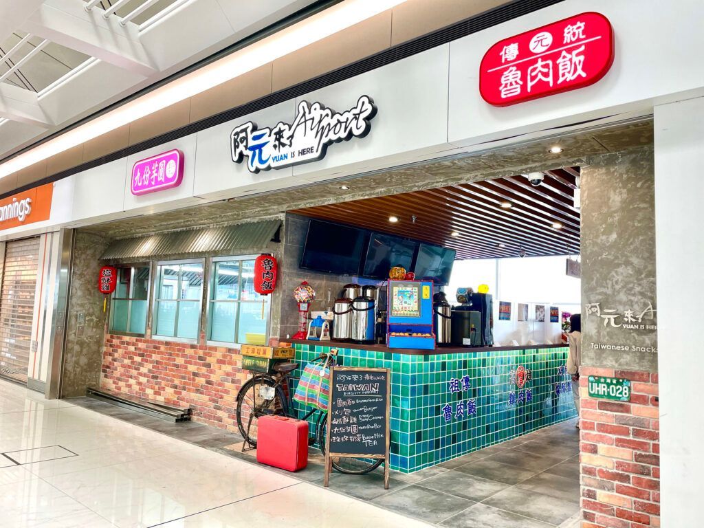 Small restaurant kiosk with a brick counter, teal railings, and bright Chinese signage in a mall corridor