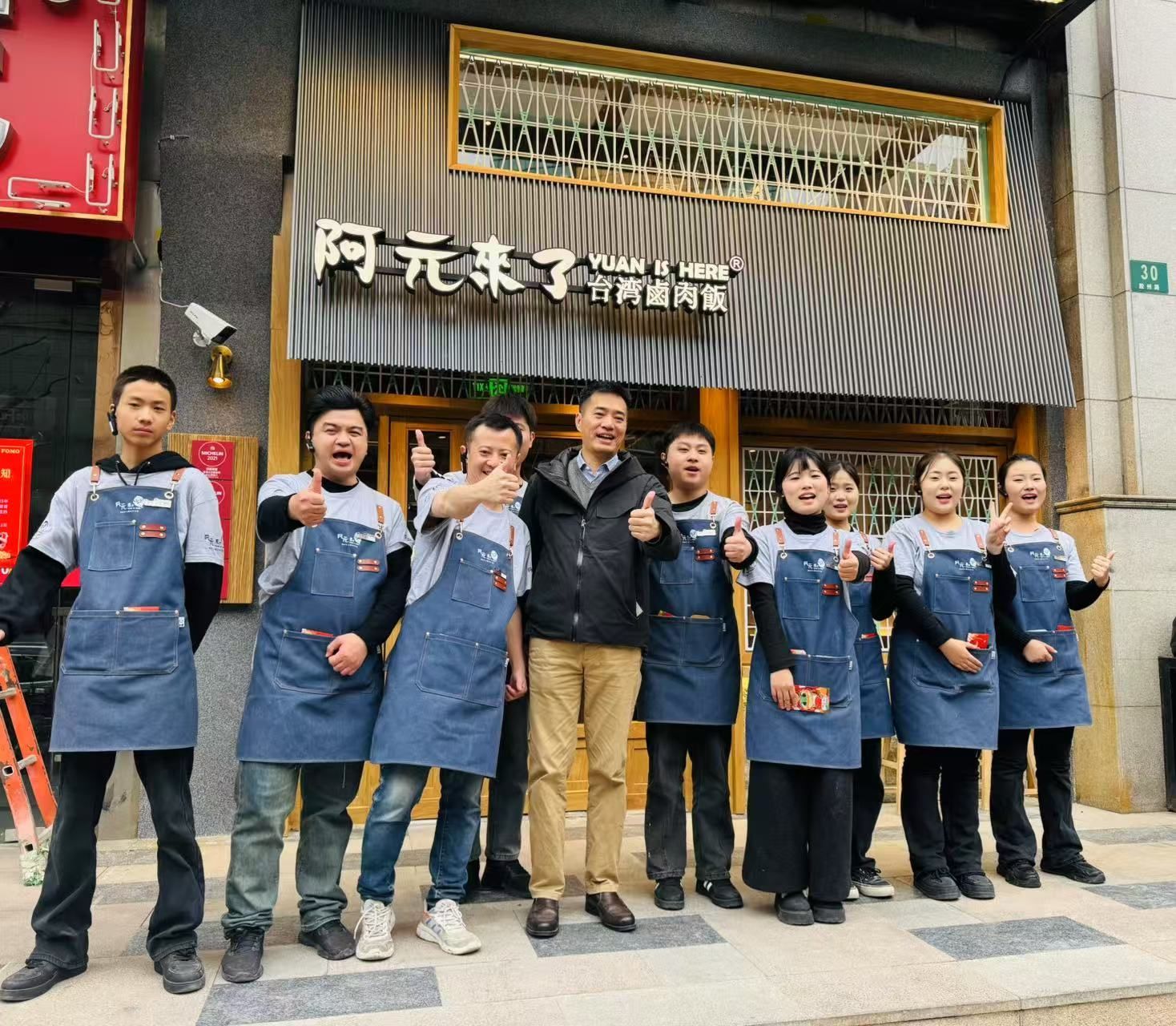 Group of people in blue aprons posing outside a restaurant with Chinese signage
