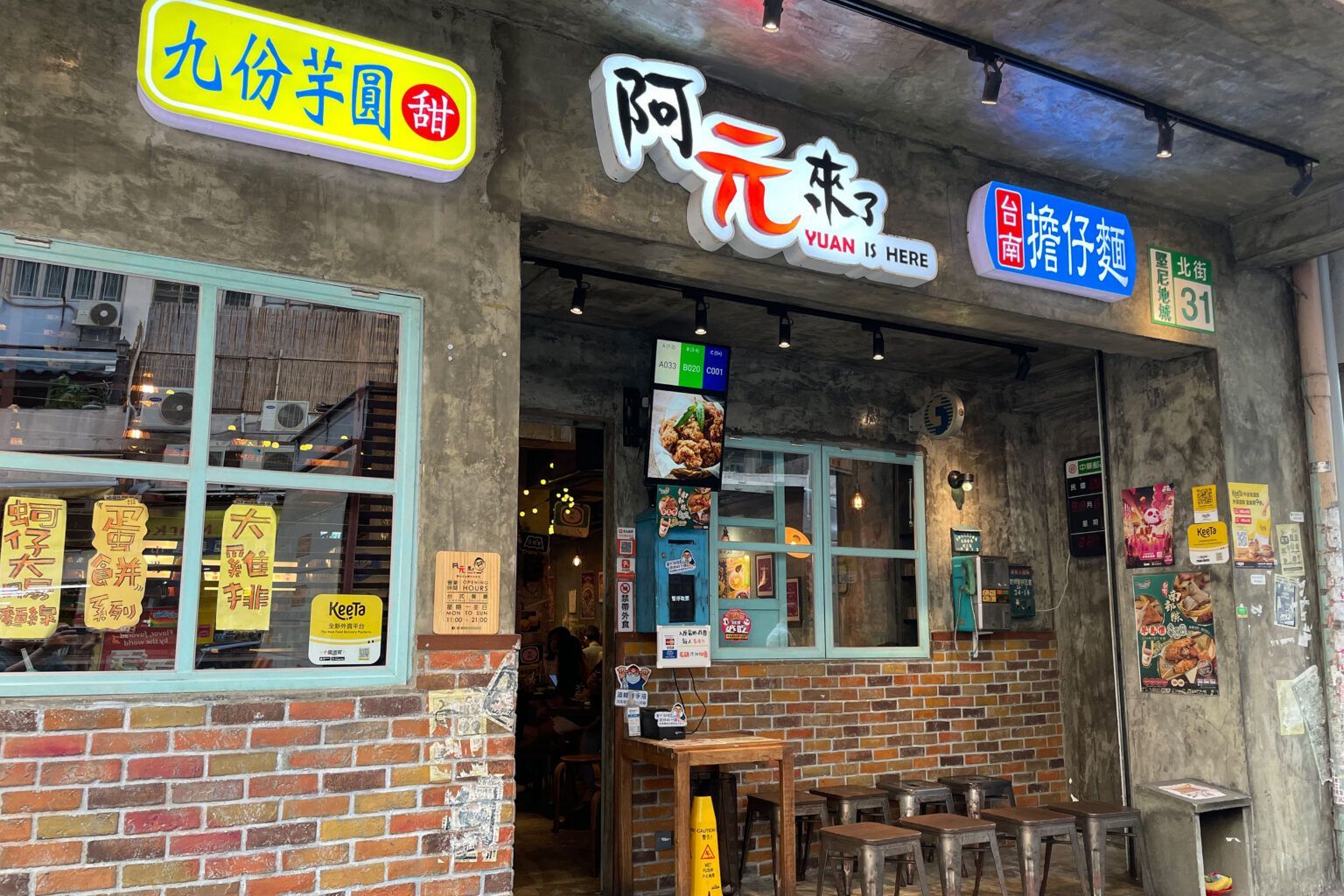 Brick storefront with Chinese signs and a small entrance, lit by hanging lights at dusk.