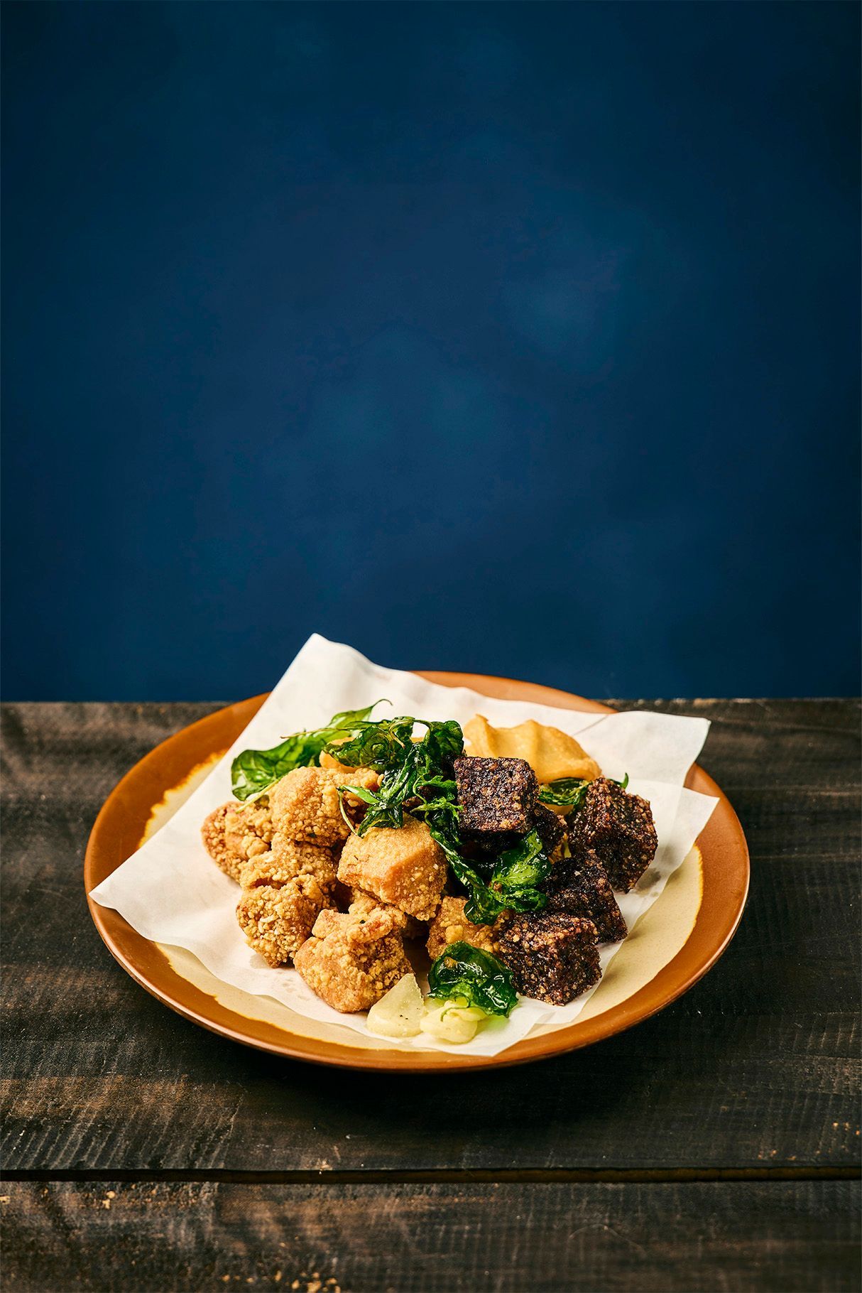 Plate of fried chicken with dark sauce on white parchment paper against a blue background