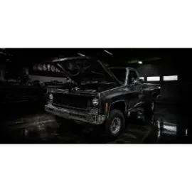 Black classic pickup truck with hood open in a dim garage, reflected on a wet floor