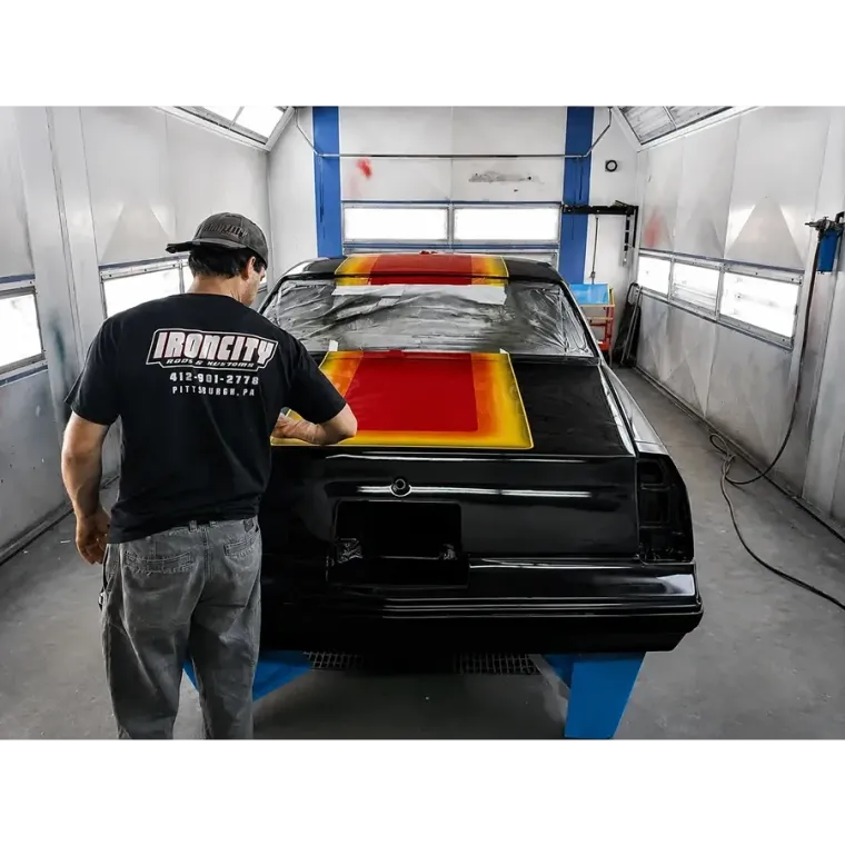 Painter spraying red and yellow stripes on a black car in a paint booth