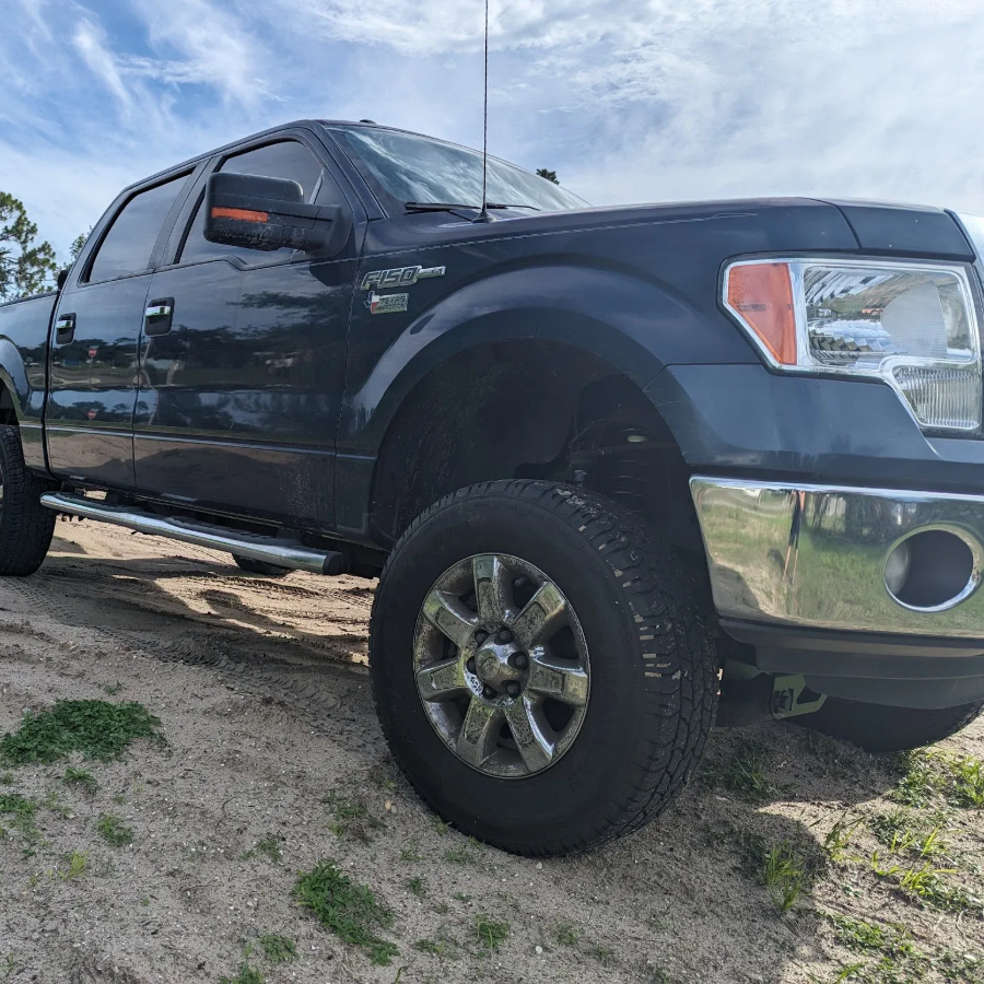 Black Ford pickup truck parked on a sandy roadside under a cloudy sky