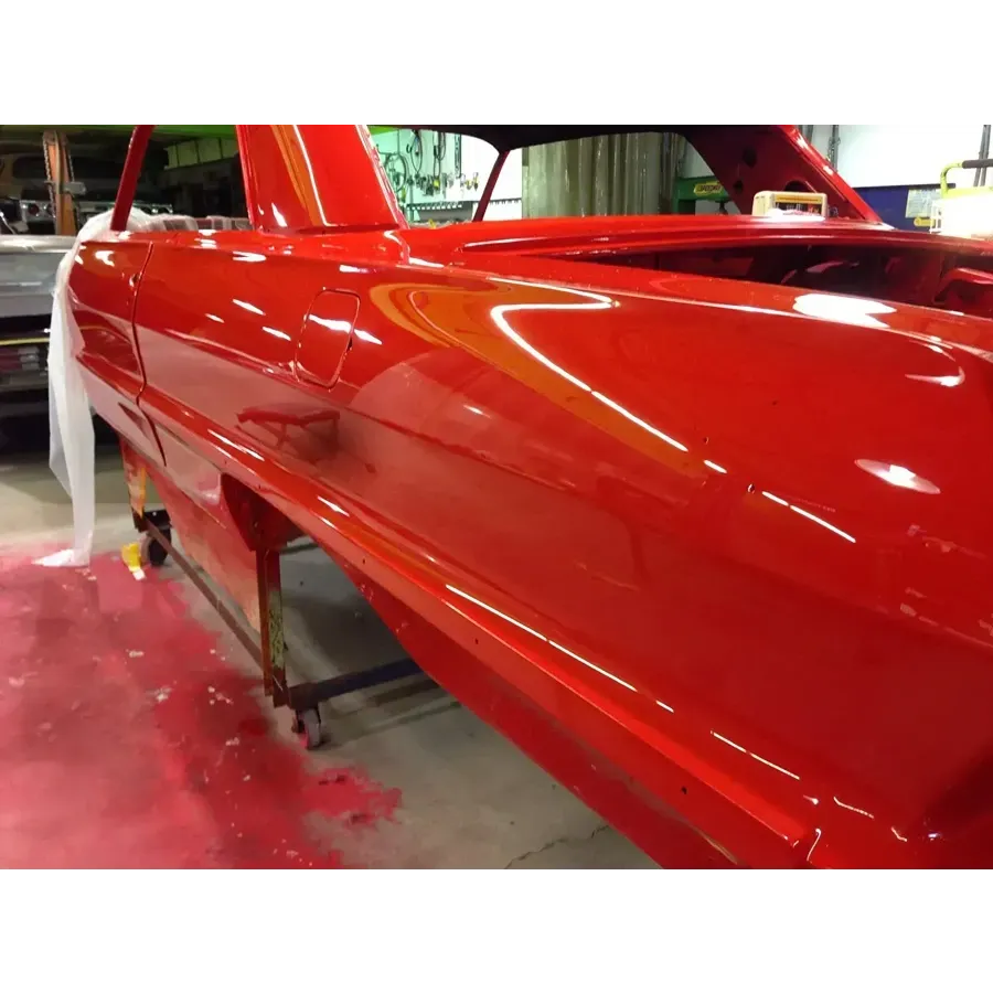 Red sports car body being spray painted glossy red in an auto body shop
