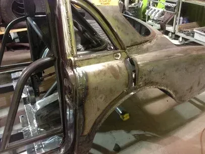 Rusty vintage car body shell in a workshop, with exposed frame and open door area