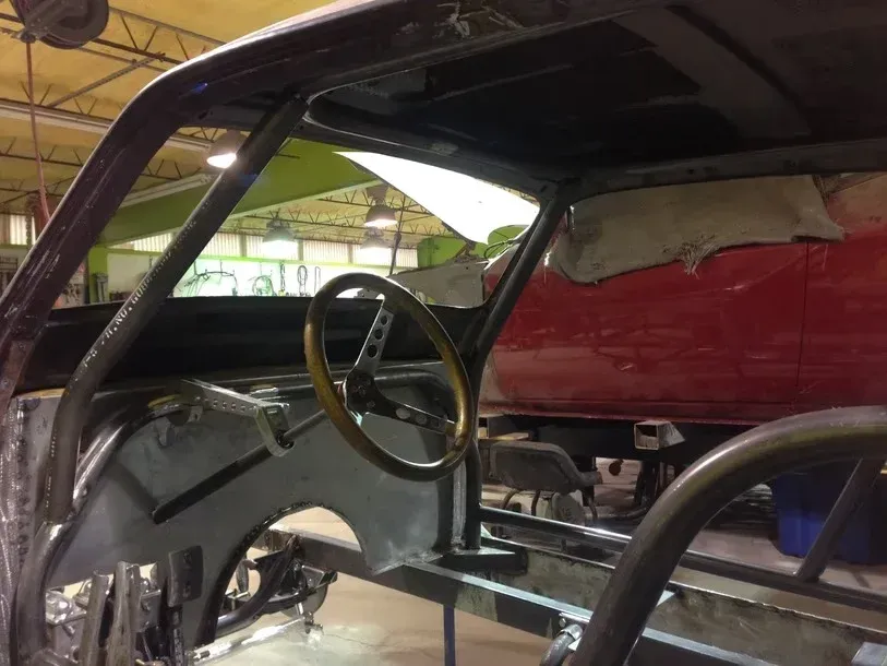 Inside a stripped car interior with exposed metal and a steering wheel, likely under restoration.
