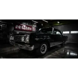 Classic black car displayed in a dim garage, with chrome details and a glossy floor reflection