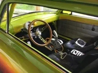 Green custom car interior with wood-rim steering wheel and black seats, viewed through the open window