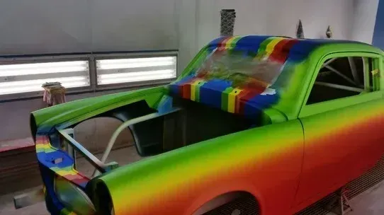 Rainbow-painted classic car in a garage, with hood open and front end under repair