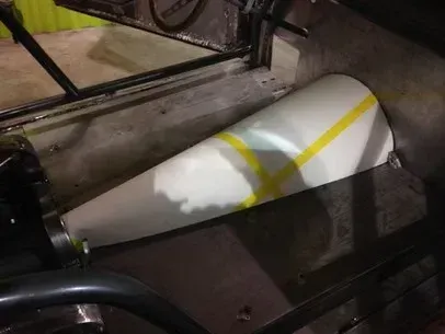 White cone-shaped object with yellow stripes resting on a metal machinery platform