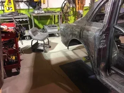 Partially stripped car body in a garage, with tools and equipment around it.