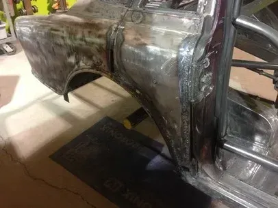 Close-up of a welded metal car body panel in a garage, with exposed frame and wheel opening