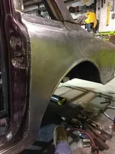 Car in a workshop with rear wheel removed, exposing the wheel well and tools underneath.