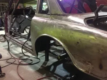 Partially stripped vintage car body in a workshop, with green primer and exposed interior panels