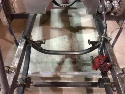 Car chassis frame with suspension parts and a red brake caliper in a workshop