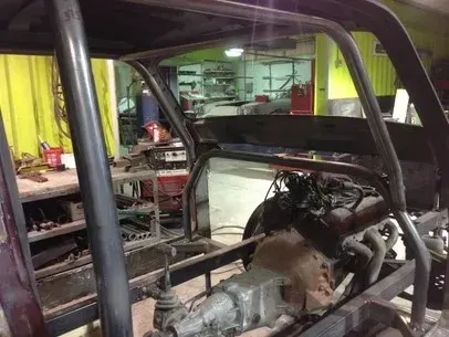 Partially assembled car chassis in a workshop with tools and equipment in the background