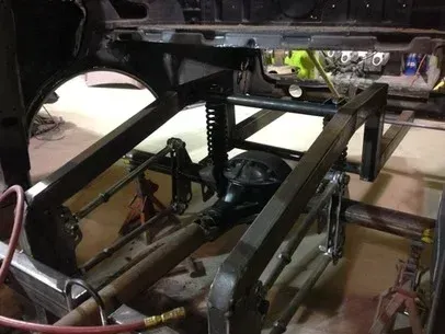 Bare metal vehicle chassis frame inside a garage, with crossbars and suspension parts visible