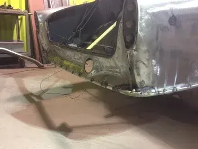 Partially restored silver car body in a workshop, with welding repairs visible on the rear section