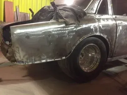 Silver vintage car body being restored in a workshop, with rear wheel and exposed frame visible