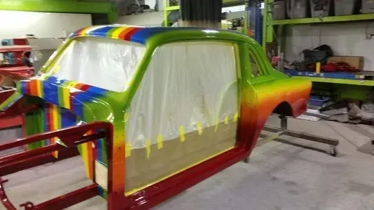 Colorfully painted car body in a workshop, masked for spray painting with plastic covering the windows.