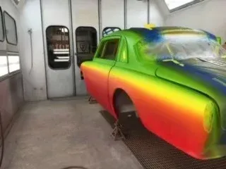 Rainbow-painted car in a spray booth, viewed from the rear side under bright lights