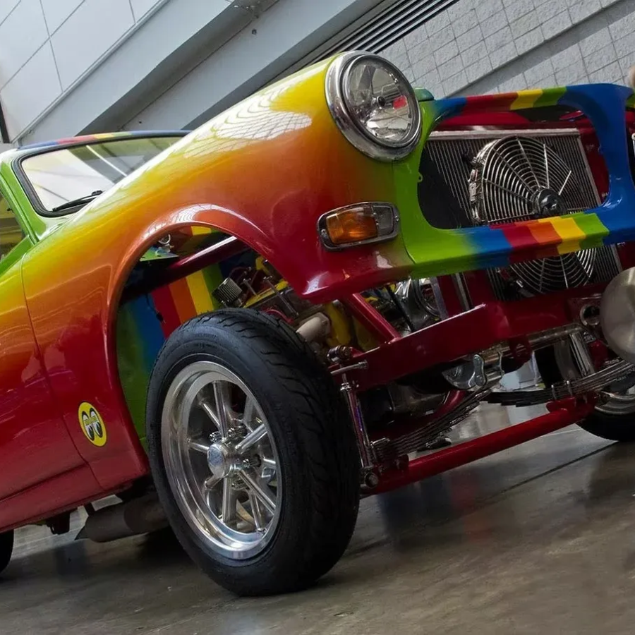 Rainbow-painted custom hot rod with chrome wheels, shown low-angle in a garage.