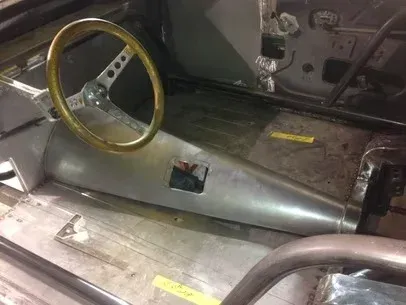 Interior of a stripped car with a metal racing steering wheel and bare floor panels